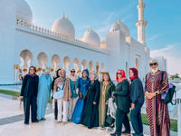 Guests in modest dress outside Sheikh Zayed Grand Mosque in the late afternoon light