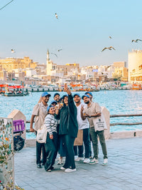 A scavenger hunt team taking a selfie by Dubai Creek, with abras and the Deira skyline behind