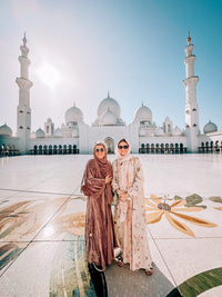 Two guests in the marble courtyard of Sheikh Zayed Grand Mosque, with its white domes and minarets behind them