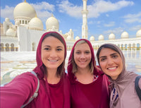 Three guests in modest dress smiling in the courtyard of Sheikh Zayed Grand Mosque