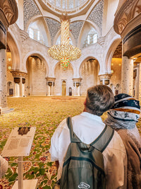 Guests in the main prayer hall of Sheikh Zayed Grand Mosque, under the crystal chandelier and on the hand-knotted carpet